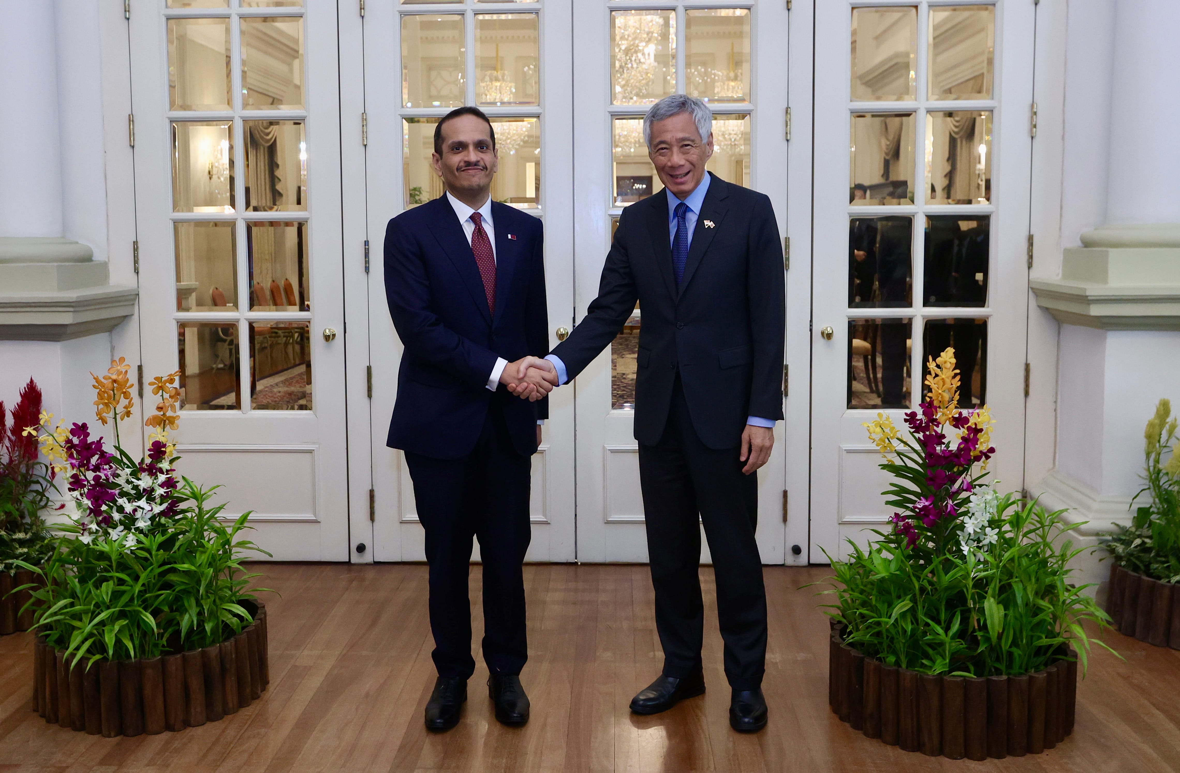 Two men in suits shaking hands in front of a glass door with flower displays.